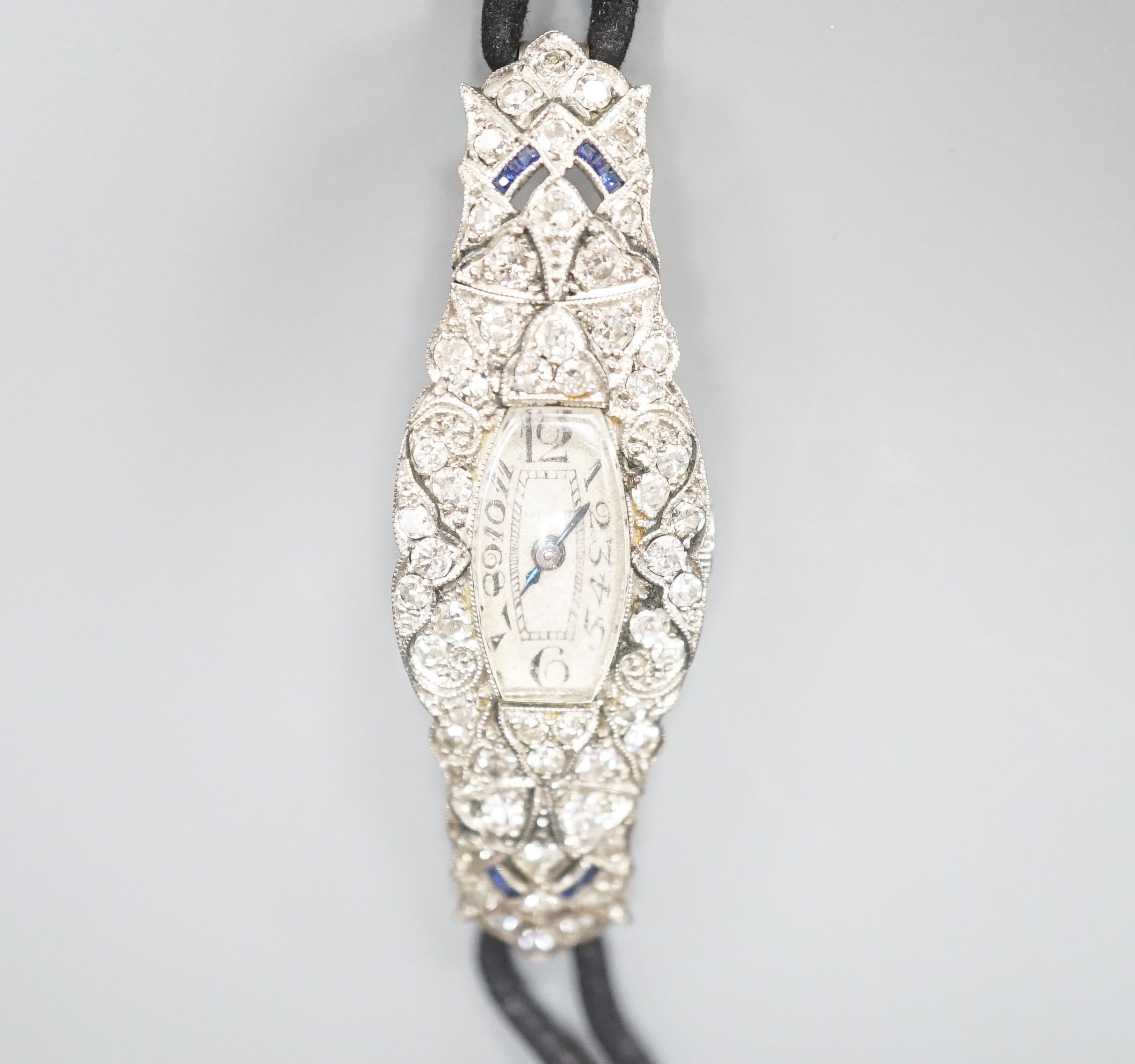 A lady's mid 20th century engraved white metal, diamond and sapphire set cocktail watch, case diameter 17mm, gross weight 18.3 grams, on a later? twin strand fabric strap.